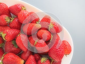 Strawberries on a plate, gray background. White dishes and delicious red large garden strawberries. Healthy food