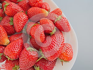 Strawberries on a plate, gray background. White dishes and delicious red large garden strawberries. Healthy food