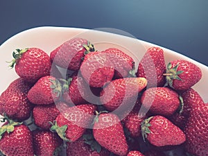Strawberries on a plate, gray background. White dishes and delicious red large garden strawberries. Healthy food