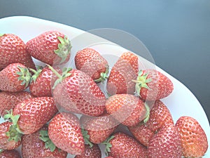 Strawberries on a plate, gray background. White dishes and delicious red large garden strawberries. Healthy food