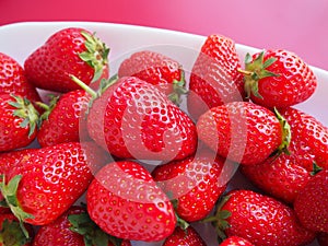 Strawberries on a plate, pink background. White dishes and ripe delicious red large garden strawberries. Healthy food