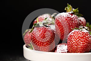 Strawberries in a plate with powdered sugar on a black background, side view close-up.