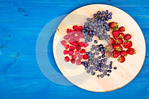 Strawberries, raspberries, blueberries and grapes on wooden plate