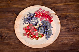 Strawberries, raspberries, blueberries and grapes on wooden plate