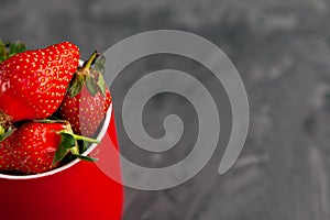 Strawberries in a red Cup on a grey concrete background