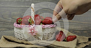 Strawberries in a small basket on the wooden table. Men`s hand takes a berry