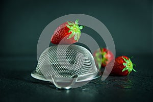 Strawberries with strainer on dark background with water drops