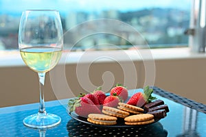 Strawberries and sweets on plate with glass of champagne or white wine on a table on balcony or terrace with blurred