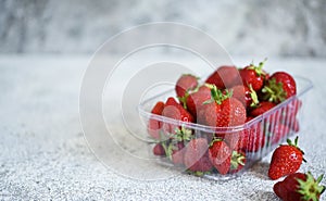 Strawberries in a tray on a concrete gray background with place for text. Horizontal focus