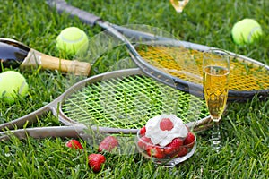 Strawberries with whipped cream, glass with champagne and tennis equipment on Wimbledon tournament grass