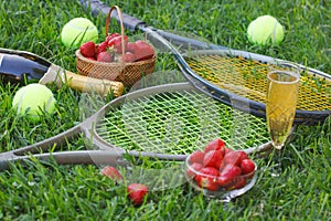 Strawberries with whipped cream, glass with champagne and tennis rackets and balls on grass