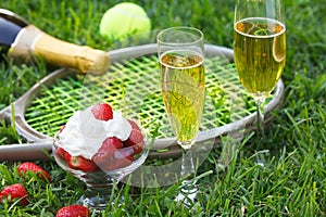 Strawberries with whipped cream, glasses with champagne and tennis equipment on Wimbledon tournament grass