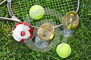 Strawberries with whipped cream, glasses with champagne and tennis equipment on Wimbledon tournament grass