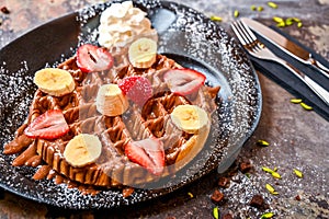 Strawberry and Banana waffle with chocolate, whipped cream, pistachio, knife and fork served in dish isolated on dark background
