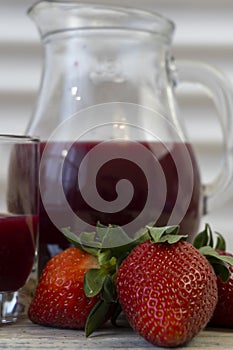 Strawberry in basket and on table on wooden background, strawberry juice in jug