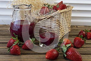 Strawberry in basket and on table on wooden background, strawberry juice in jug