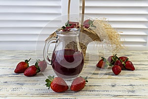 Strawberry in basket and on table on wooden background, strawberry juice in jug