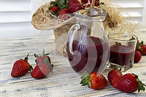 Strawberry in basket and on table on wooden background, strawberry juice in jug