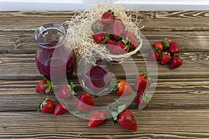 Strawberry in basket and on table on wooden background, strawberry juice in jug