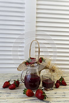 Strawberry in basket and on table on wooden background, strawberry juice in jug