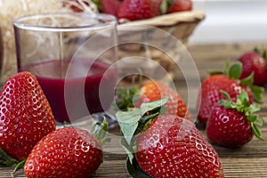 Strawberry in basket and on table on wooden background, strawberry juice in jug