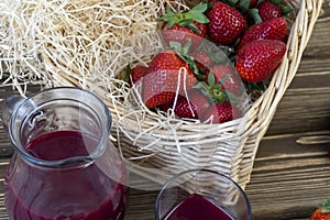 Strawberry in basket and on table on wooden background, strawberry juice in jug