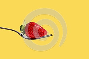 Strawberry berry with green leaves lying on the fork. Yellow background photo