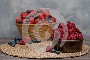 Strawberry and blueberry in basket and raspberries in bowl on wood table. Fresh berries.