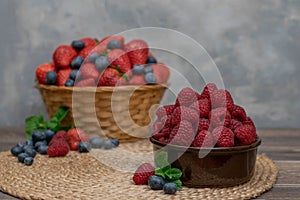 Strawberry and blueberry in basket and raspberries in bowl on wood table. Fresh berries