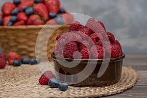 Strawberry and blueberry in basket and raspberries in bowl on wood table. Fresh berries