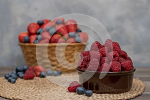Strawberry and blueberry in basket and raspberries in bowl on wood table. Fresh berries.