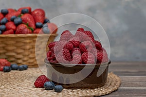 Strawberry and blueberry in basket and raspberries in bowl on wood table. Fresh berries.