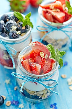 Strawberry blueberry yogurt parfait with addition of muesli, coconut flakes and fresh mint