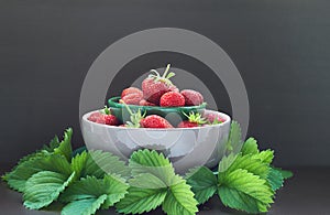Strawberry in bowl isolated on black background, composition from berries and fresh leaves