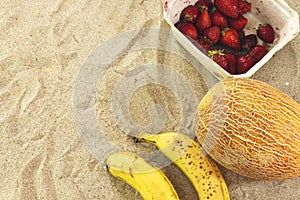 Strawberry box and melon, two bananas in sand