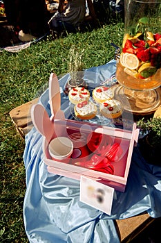 Strawberry cakes, large glass lemonade maker with fruit drink, paper cups in the basket