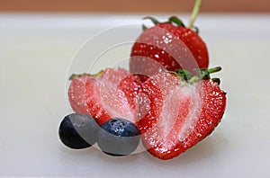 Strawberry and chopped strawberry with berry fruit on the white floor.