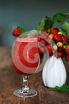 Strawberry cocktail in misted glass and white ceramic vase with ripe red strawberry branches