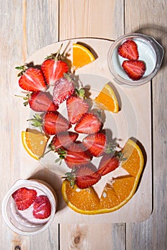 Strawberry cut in half, orange sliced â€‹â€‹jars of yogurt, two spoons on a wooden table