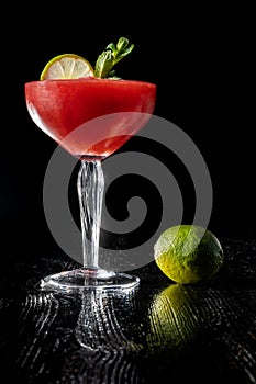 Strawberry daiquiri cocktail with lime, strawberry syrop, cherry and mint on black background.