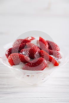 Strawberry dessert in a plate with ice cream and cream on a white wooden background
