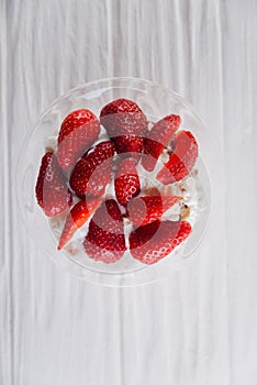 Strawberry dessert in a plate with ice cream and cream on a white wooden background