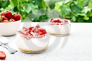 Strawberry desserts with fresh strawberries, cream cheese or natural yoghurt and oat granola in glass jars on light surface and