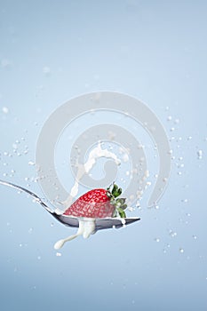 Strawberry dropping into a spoon with milk creating splashes and drops on blue background