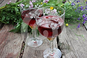 Strawberry elderflower cocktail, and wild blue and yellow flowers on the wooden board table. Two glasses of red wine with berries