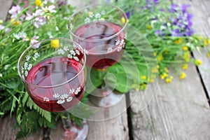 Strawberry elderflower cocktail, and wild blue and yellow flowers on the wooden board table. Two glasses of red wine with berries