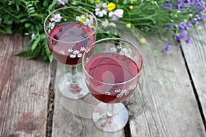 Strawberry elderflower cocktail, and wild blue and yellow flowers on the wooden board table. Two glasses of red wine with berries