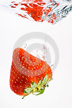 Strawberry falls deeply under water with a big splash. Fruit sinking in clear water on white background