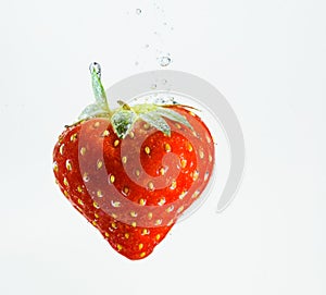 Strawberry falls deeply under water with a big splash. Fruit sinking in clear water on white background
