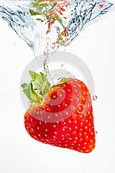 Strawberry falls deeply under water with a big splash. Fruit sinking in clear water on white background